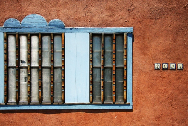 A pale, weathered blue window frame on an adobe wall in Albuquerque